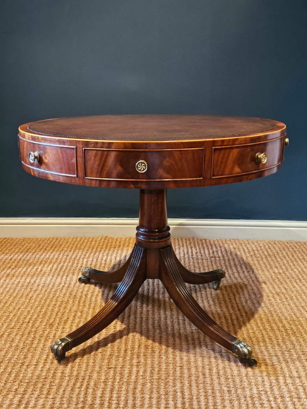 A small circular Regency mahogany drum table with a brown leather inset top, frieze drawers, turned pedestal stem, and reeded splayed legs on brass castors. View XI