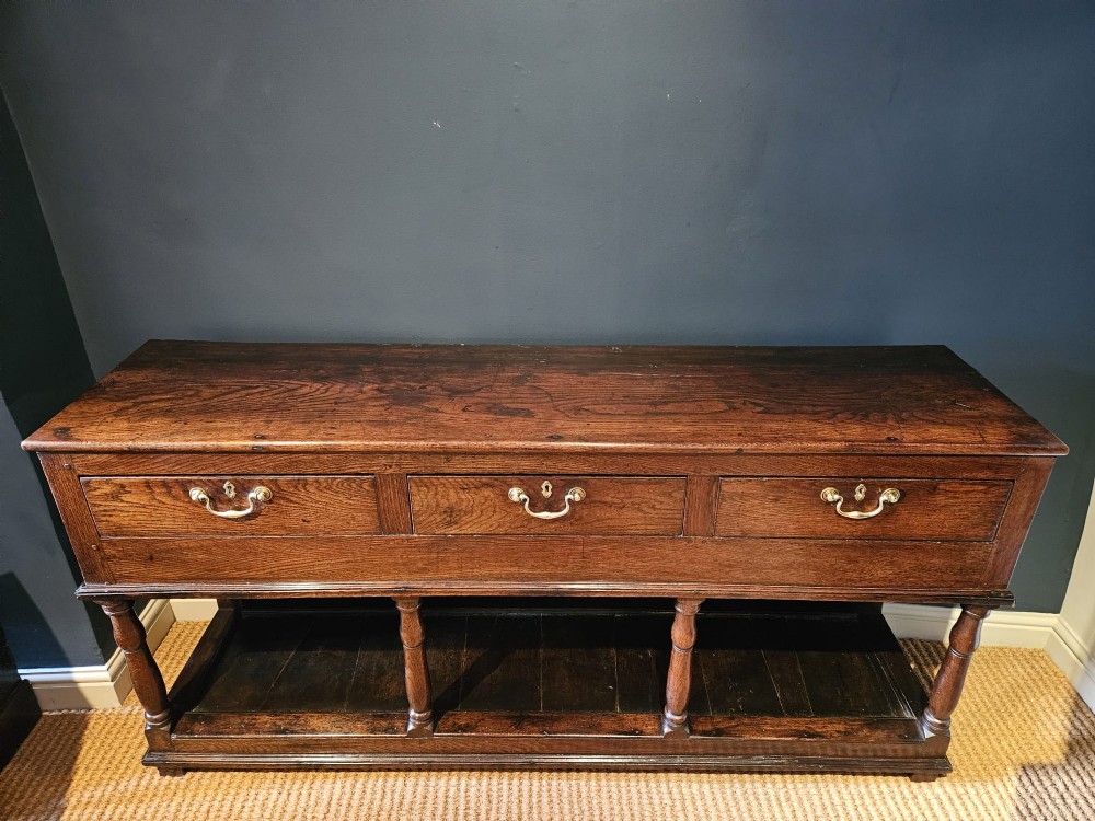 An 18th-century George II oak pot board dresser featuring three frieze drawers with brass handles set above an open lower shelf and turned baluster supports. View X