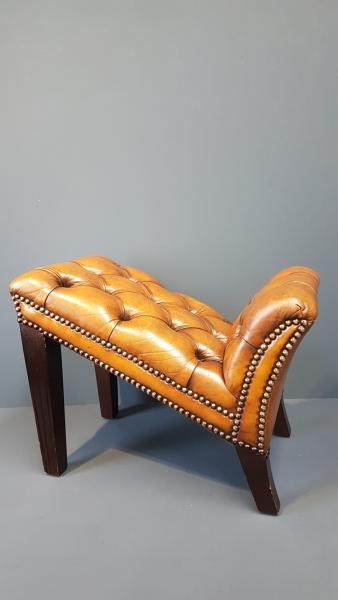 A 1930s tan leather footstool featuring an inclined top with deep buttoning, brass stud trim, and dark wooden legs. View II