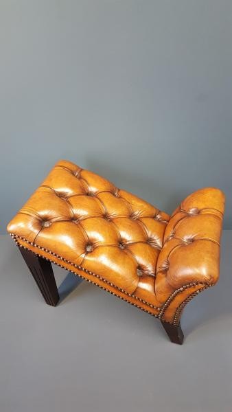A 1930s tan leather footstool featuring an inclined top with deep buttoning, brass stud trim, and dark wooden legs. View III