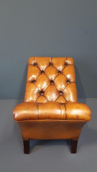 A 1930s tan leather footstool featuring an inclined top with deep buttoning, brass stud trim, and dark wooden legs. View IV