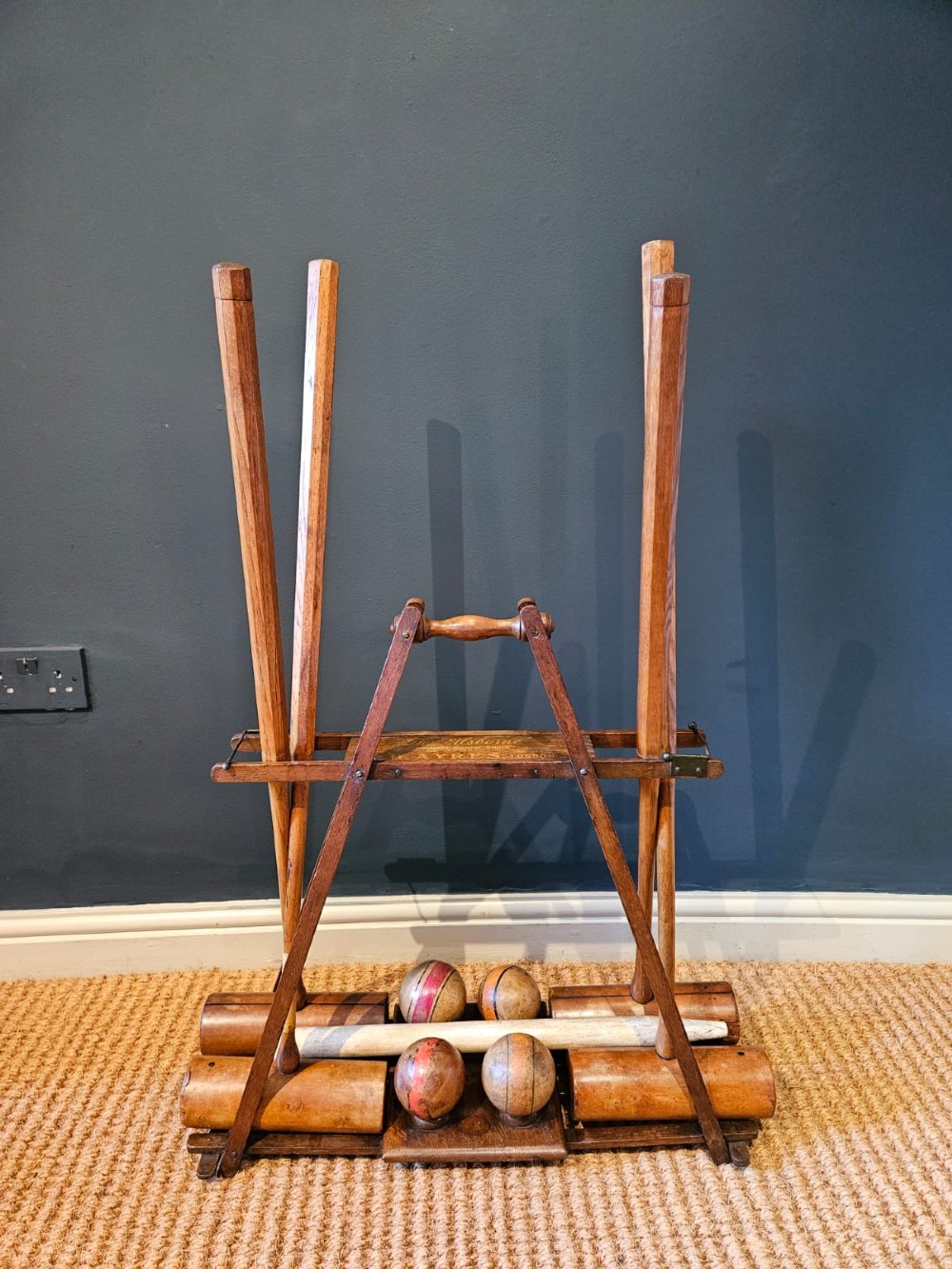 An Edwardian wooden croquet stand featuring four tall wooden mallets and painted croquet balls supported on a timber frame with a central turned carrying handle.