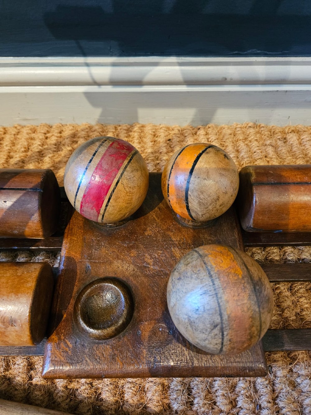 An Edwardian wooden croquet stand featuring four tall wooden mallets and painted croquet balls supported on a timber frame with a central turned carrying handle. View II