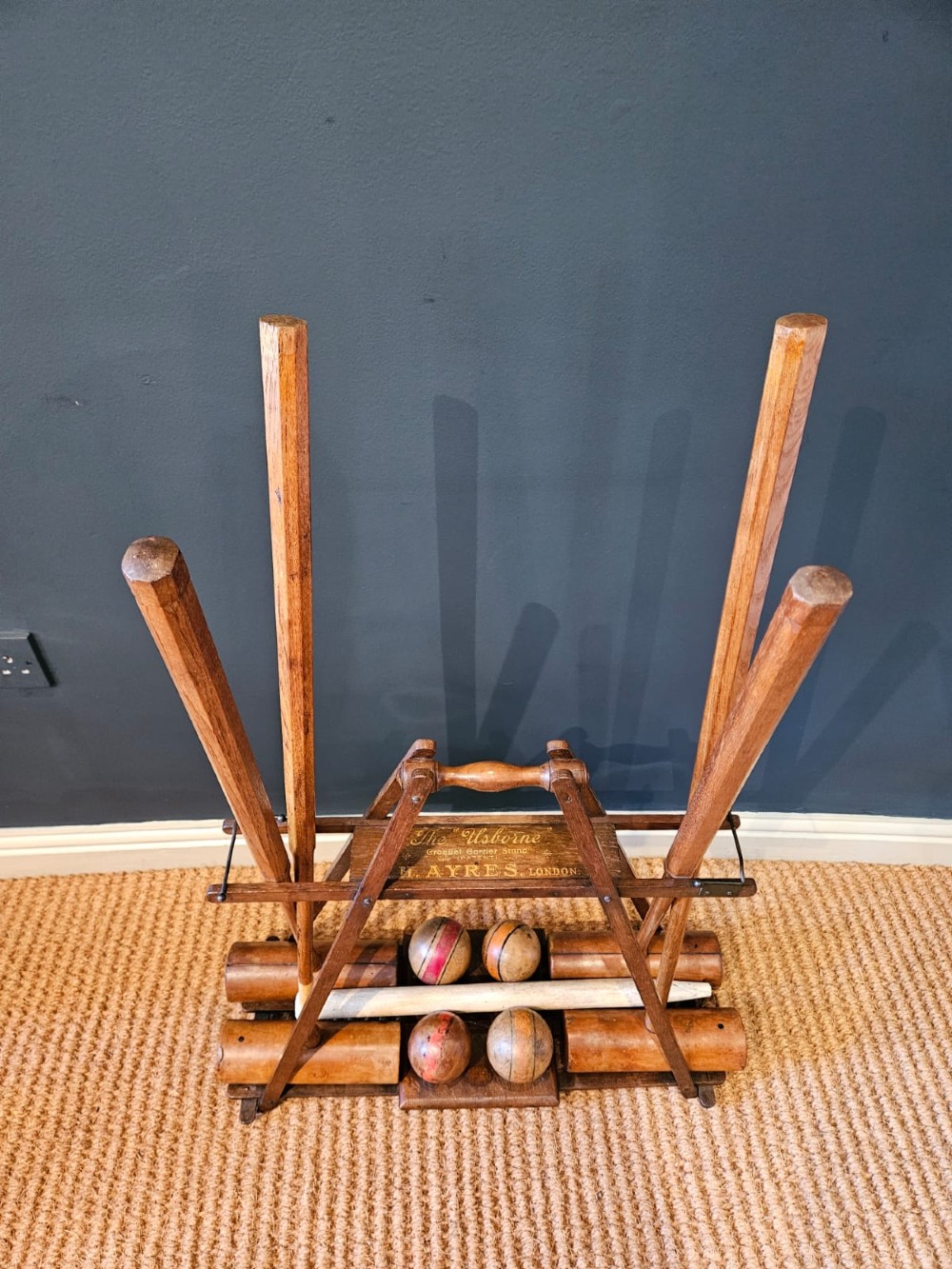An Edwardian wooden croquet stand featuring four tall wooden mallets and painted croquet balls supported on a timber frame with a central turned carrying handle. View III