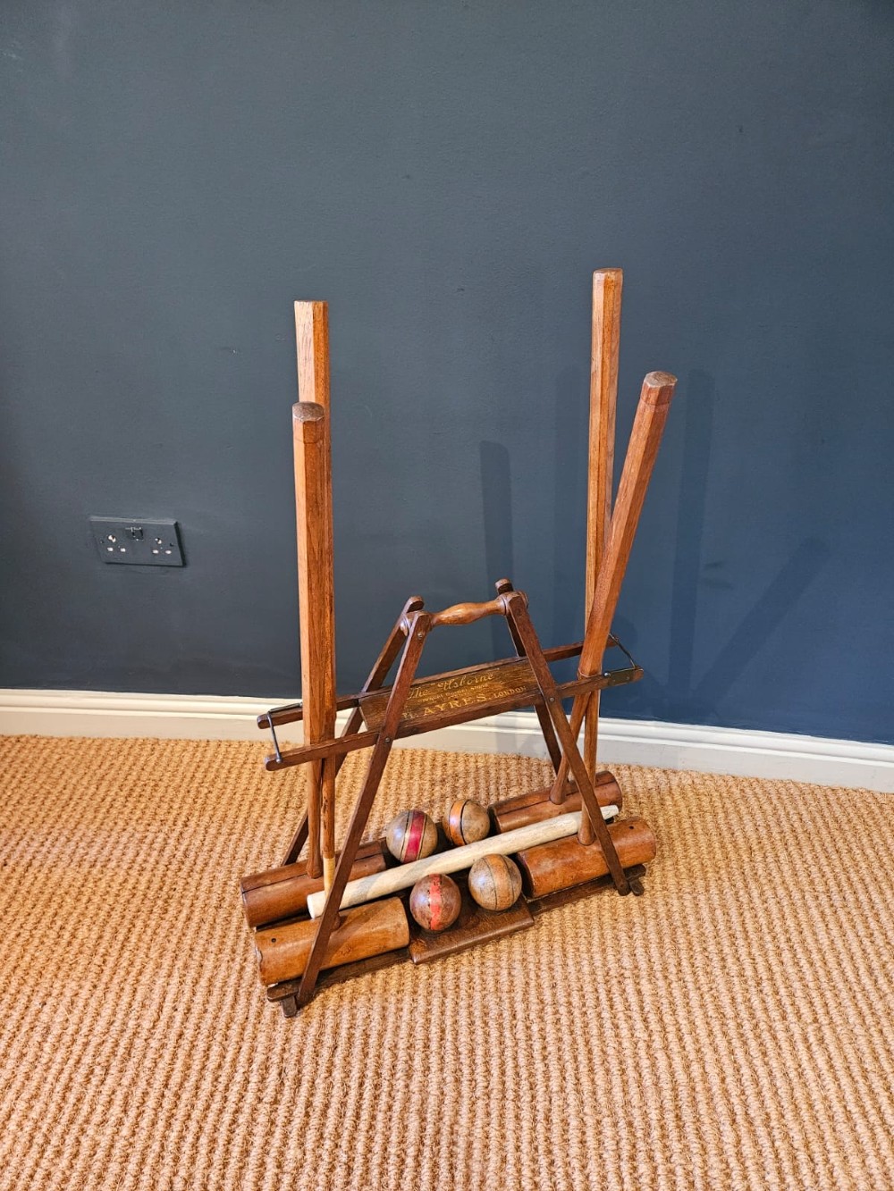 An Edwardian wooden croquet stand featuring four tall wooden mallets and painted croquet balls supported on a timber frame with a central turned carrying handle. View V