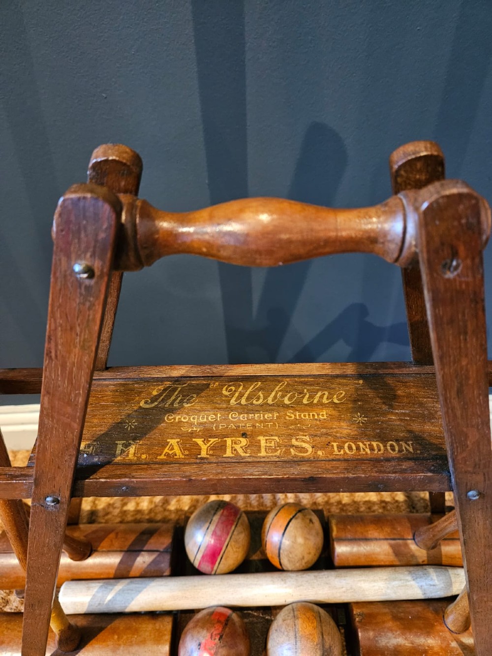 An Edwardian wooden croquet stand featuring four tall wooden mallets and painted croquet balls supported on a timber frame with a central turned carrying handle. View VI