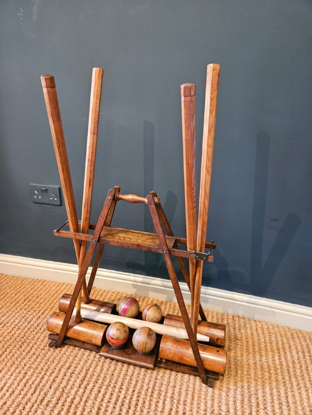 An Edwardian wooden croquet stand featuring four tall wooden mallets and painted croquet balls supported on a timber frame with a central turned carrying handle. View VII