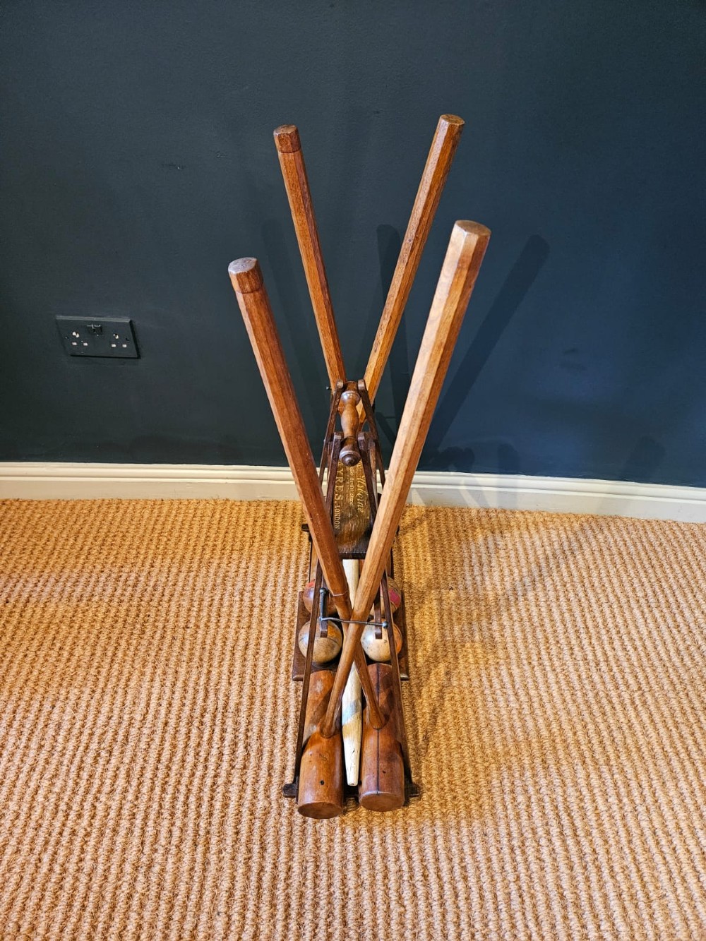 An Edwardian wooden croquet stand featuring four tall wooden mallets and painted croquet balls supported on a timber frame with a central turned carrying handle. View IX