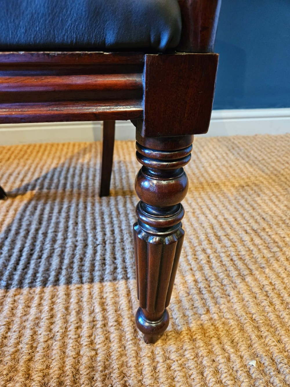 A 19th-century William IV dark mahogany desk chair featuring dynamic scroll arms, turned reeded front legs, and a black leather upholstered seat. View IV