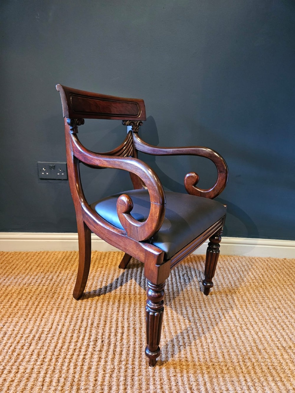 A 19th-century William IV dark mahogany desk chair featuring dynamic scroll arms, turned reeded front legs, and a black leather upholstered seat. View VI