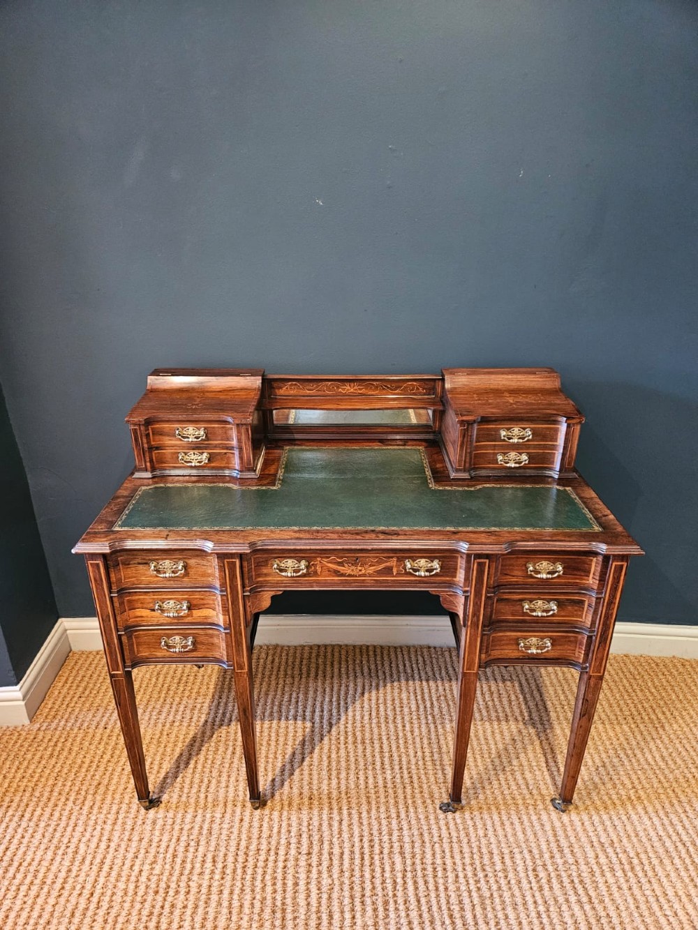 An Edwardian inlaid rosewood writing desk featuring a central green leather writing surface, raised side drawers, and tapered square legs.