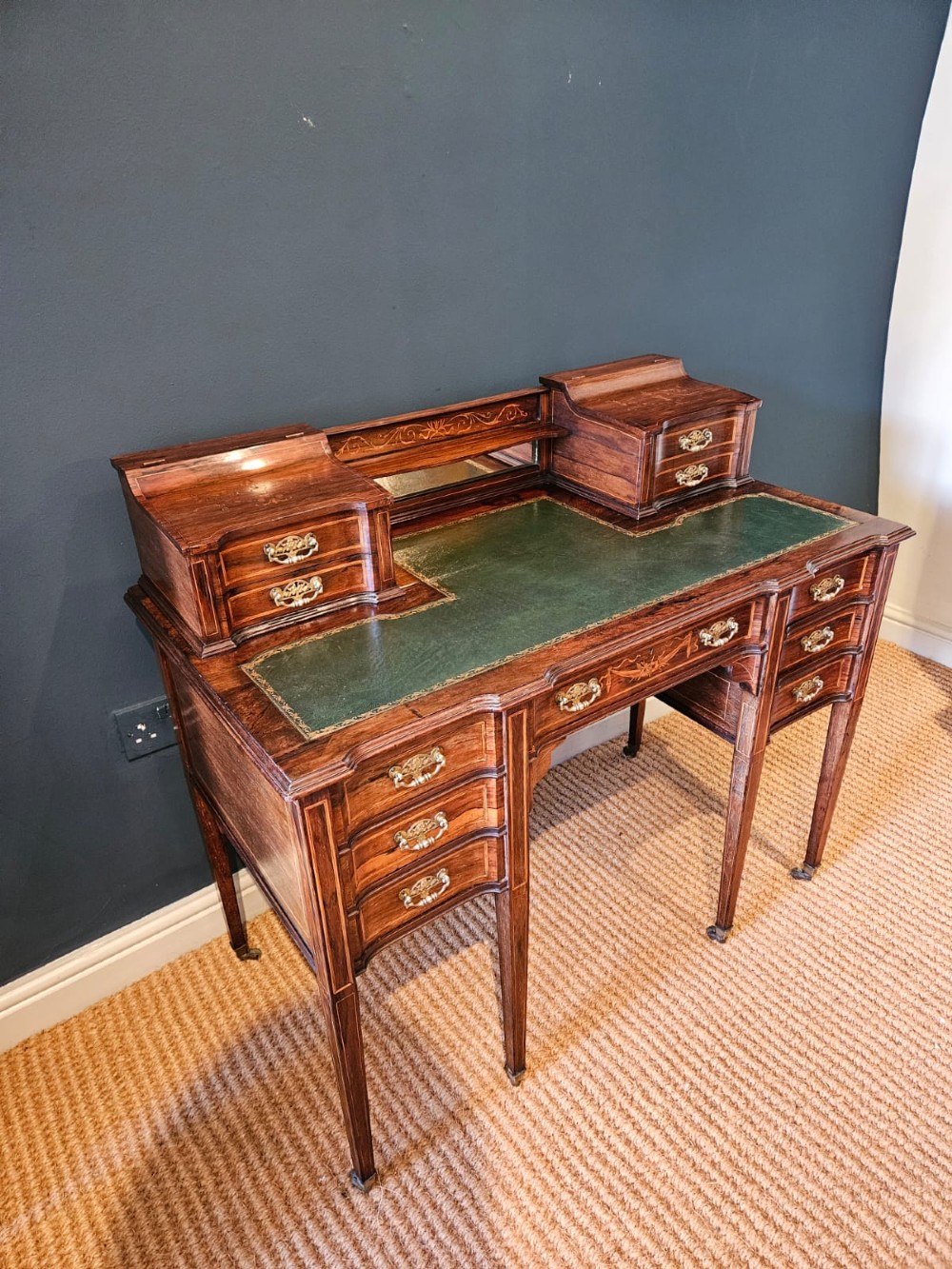An Edwardian inlaid rosewood writing desk featuring a central green leather writing surface, raised side drawers, and tapered square legs. View V