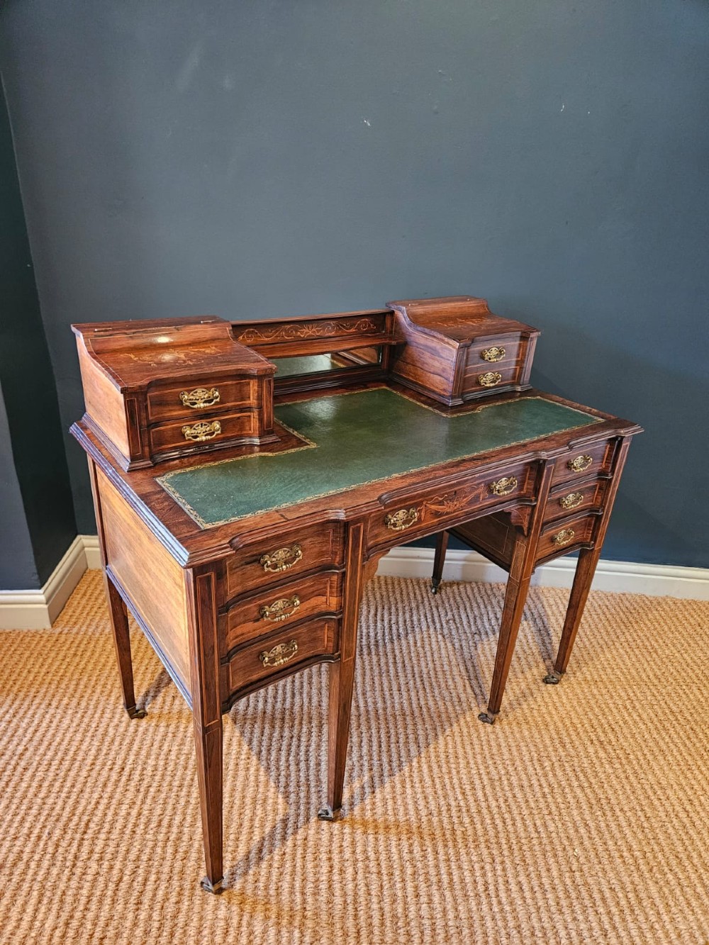 An Edwardian inlaid rosewood writing desk featuring a central green leather writing surface, raised side drawers, and tapered square legs. View VII