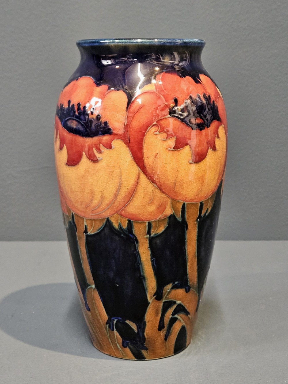 An Art Deco Moorcroft earthenware vase decorated with tube-lined orange poppy flowers on a deep cobalt blue background. View II