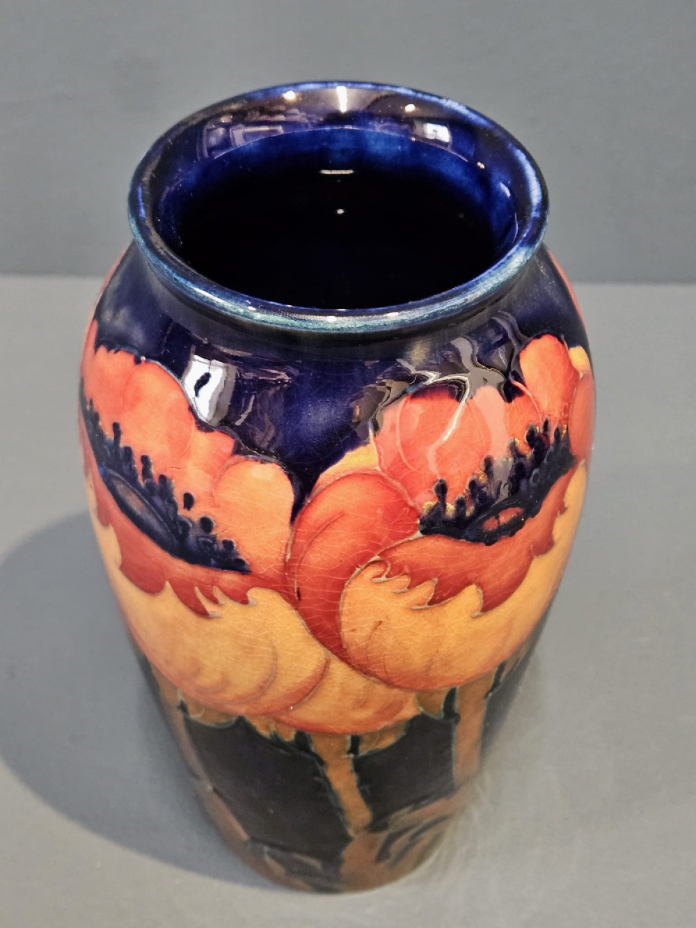 An Art Deco Moorcroft earthenware vase decorated with tube-lined orange poppy flowers on a deep cobalt blue background. View III