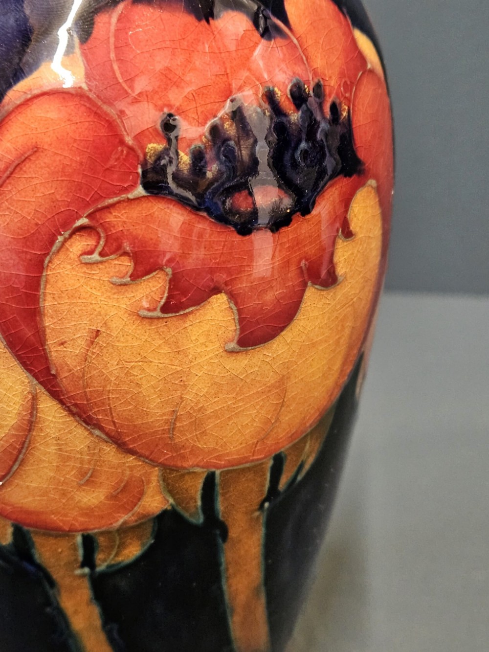 An Art Deco Moorcroft earthenware vase decorated with tube-lined orange poppy flowers on a deep cobalt blue background. View IV