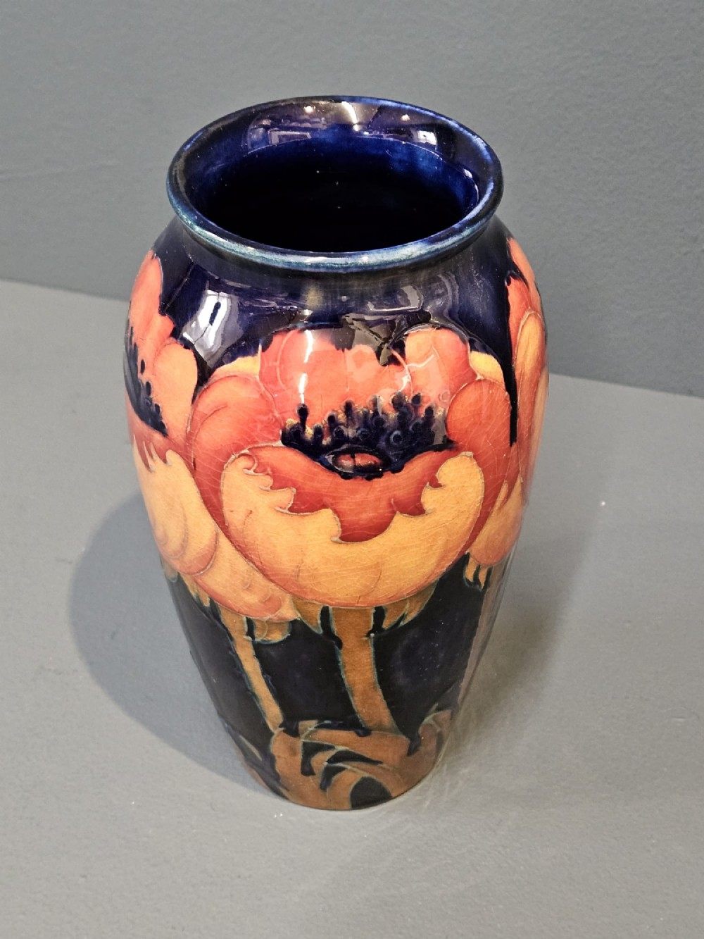 An Art Deco Moorcroft earthenware vase decorated with tube-lined orange poppy flowers on a deep cobalt blue background. View VI