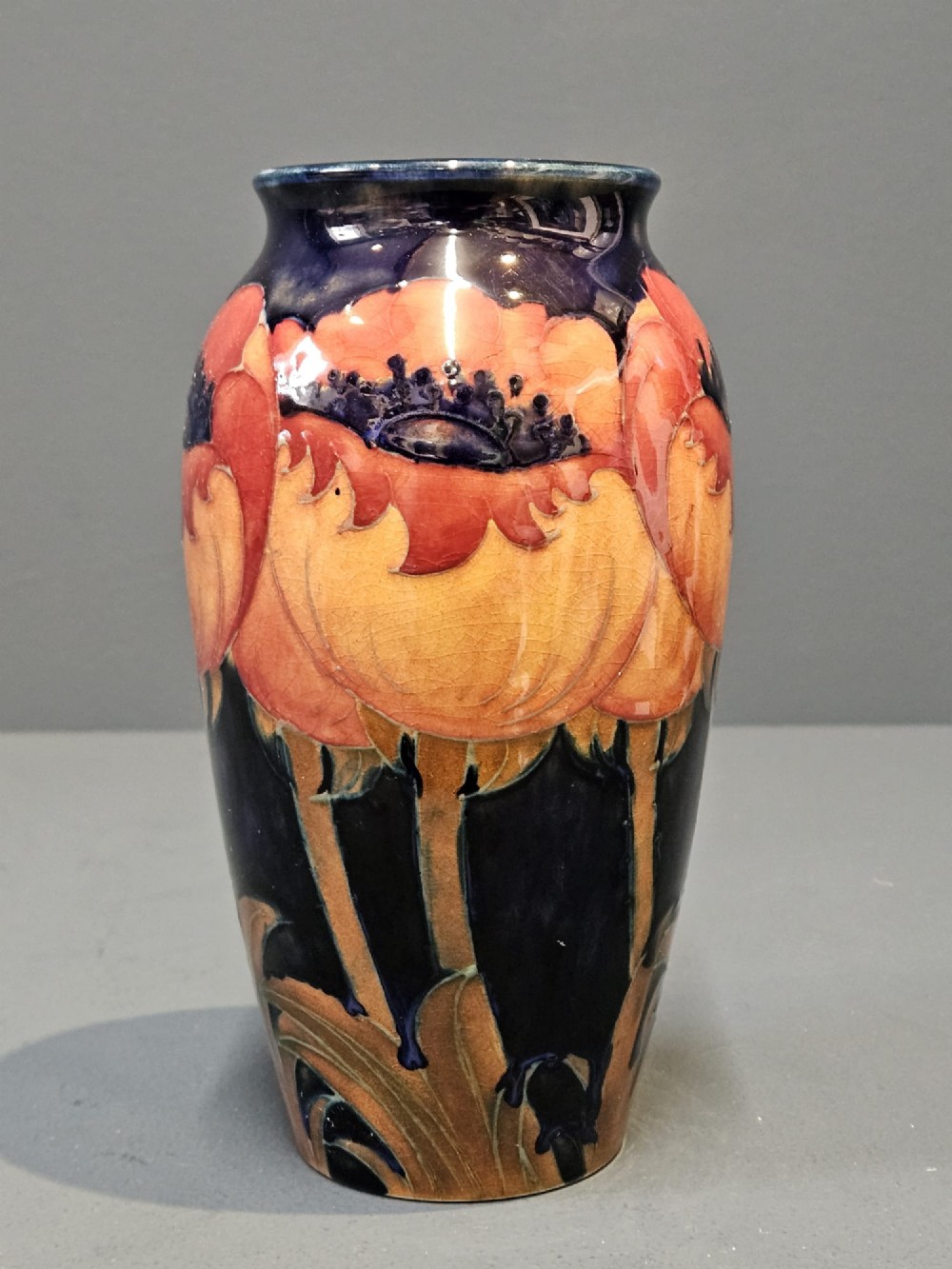 An Art Deco Moorcroft earthenware vase decorated with tube-lined orange poppy flowers on a deep cobalt blue background. View VII