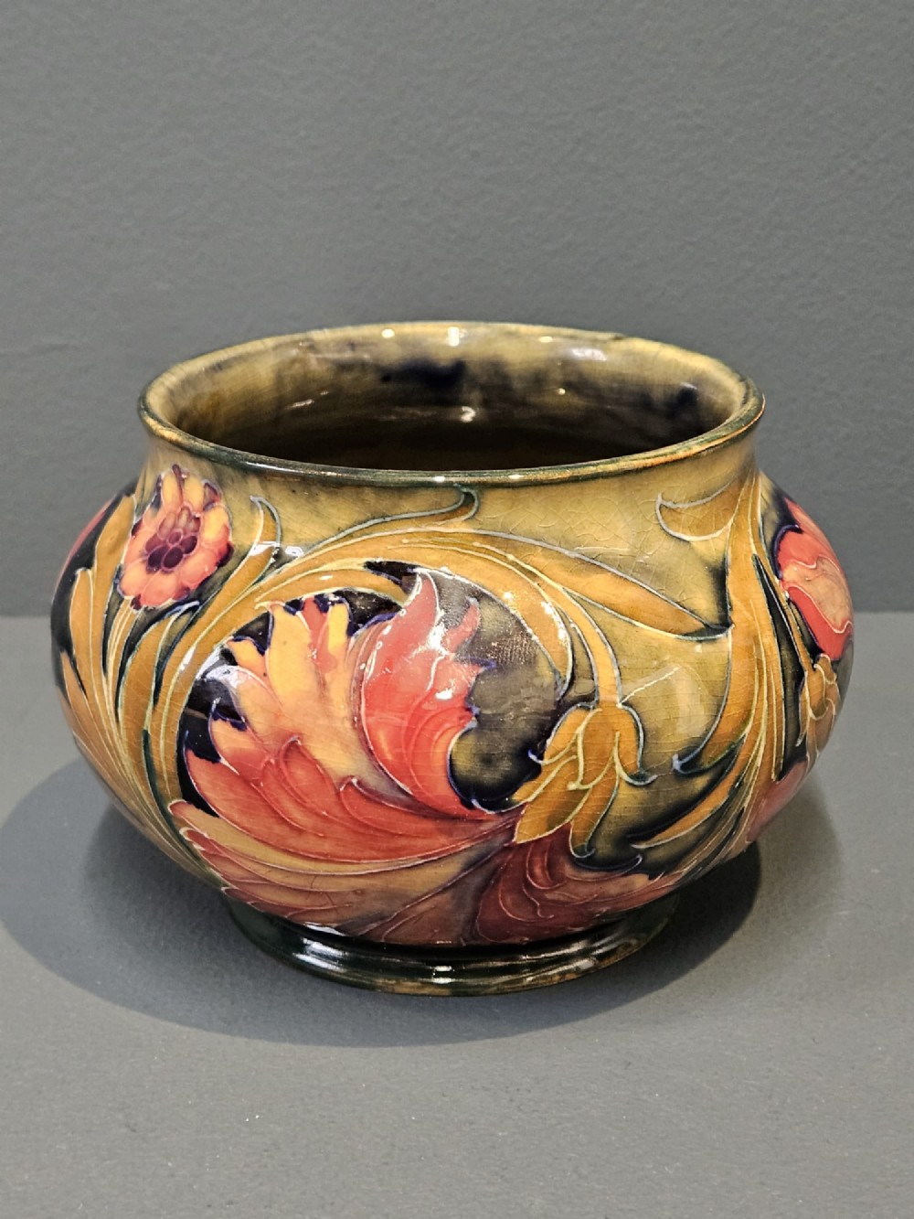 A squat ceramic vase decorated with Art Nouveau tube-lined floral motifs in ochre yellow, terracotta, and dark green glazes.
