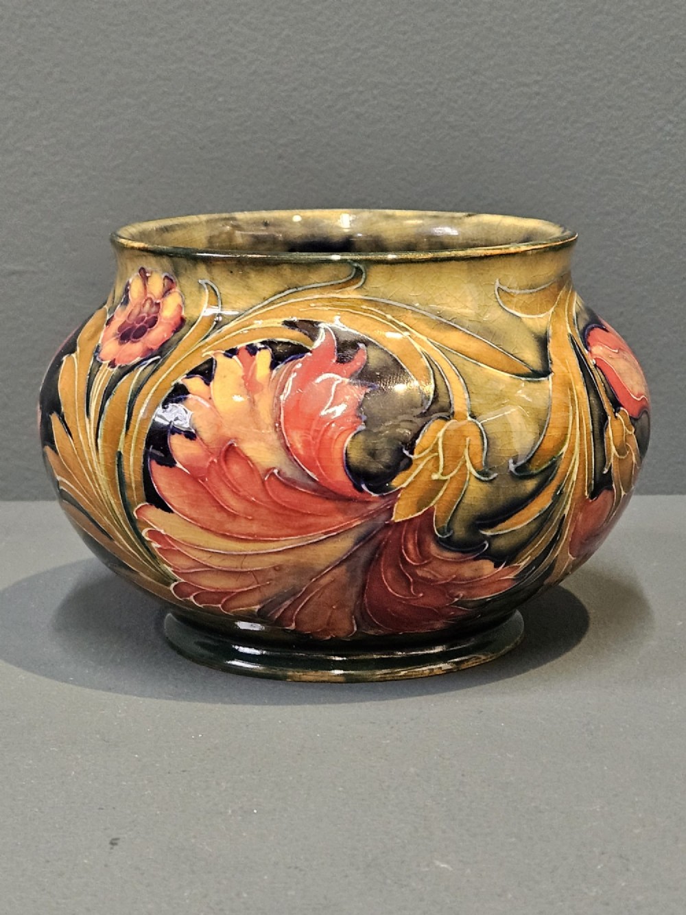 A squat ceramic vase decorated with Art Nouveau tube-lined floral motifs in ochre yellow, terracotta, and dark green glazes. View II