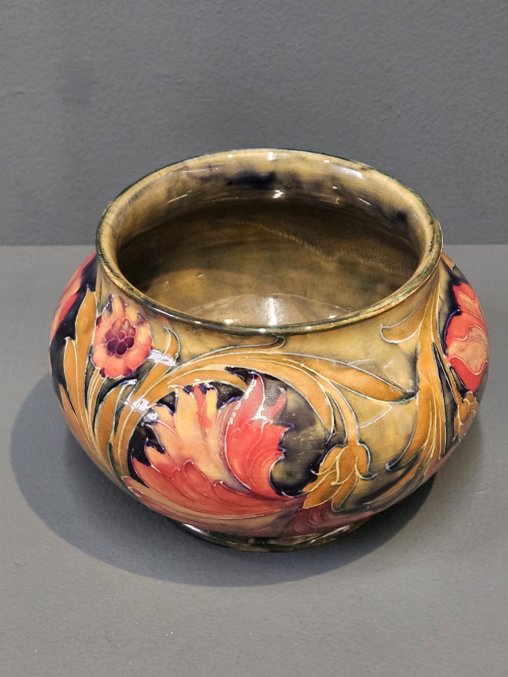 A squat ceramic vase decorated with Art Nouveau tube-lined floral motifs in ochre yellow, terracotta, and dark green glazes. View III