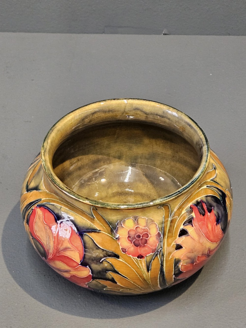 A squat ceramic vase decorated with Art Nouveau tube-lined floral motifs in ochre yellow, terracotta, and dark green glazes. View V
