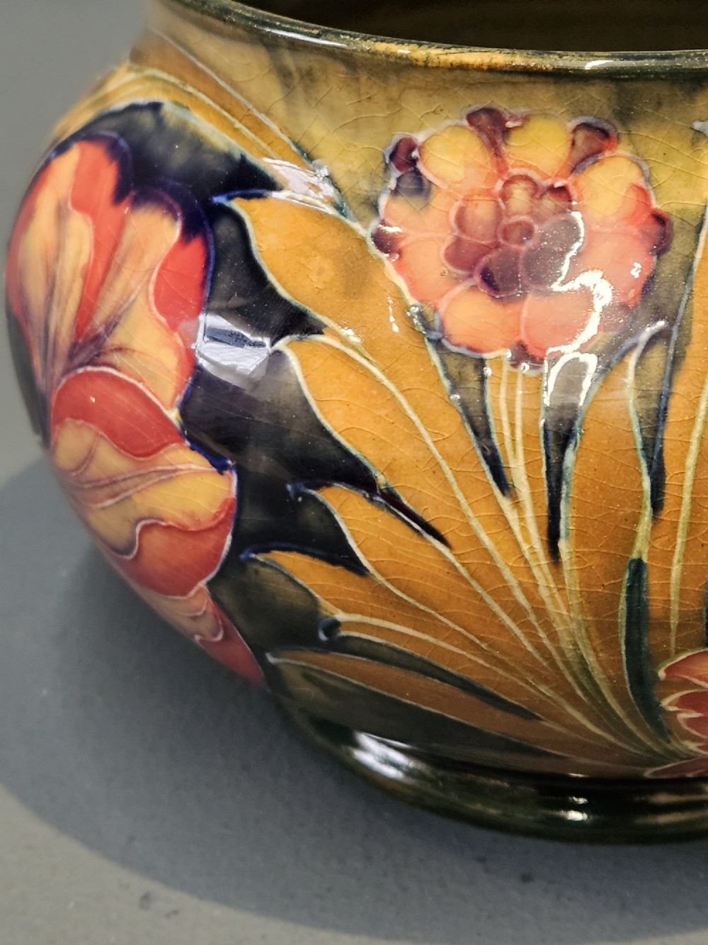 A squat ceramic vase decorated with Art Nouveau tube-lined floral motifs in ochre yellow, terracotta, and dark green glazes. View VI