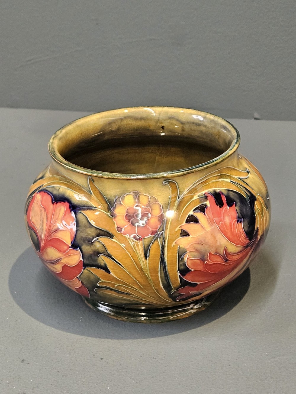A squat ceramic vase decorated with Art Nouveau tube-lined floral motifs in ochre yellow, terracotta, and dark green glazes. View VII