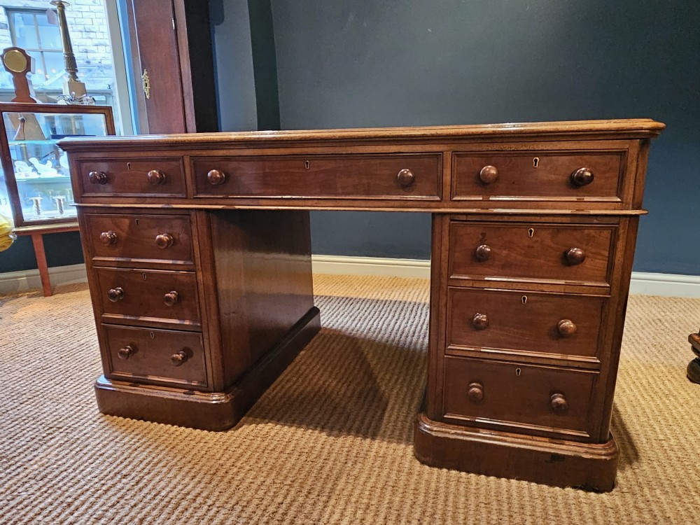 A Mid-Victorian mahogany partners desk featuring a pedestal layout with nine drawers on the front, turned timber knobs, and a solid plinth base.