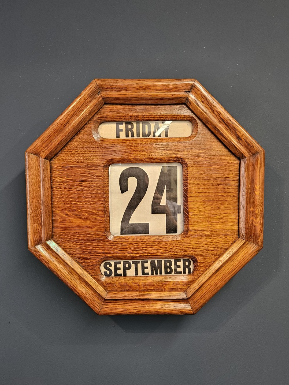 An octagonal Edwardian oak perpetual wall calendar with glazed apertures displaying the day, numerical date, and month on printed rollers.