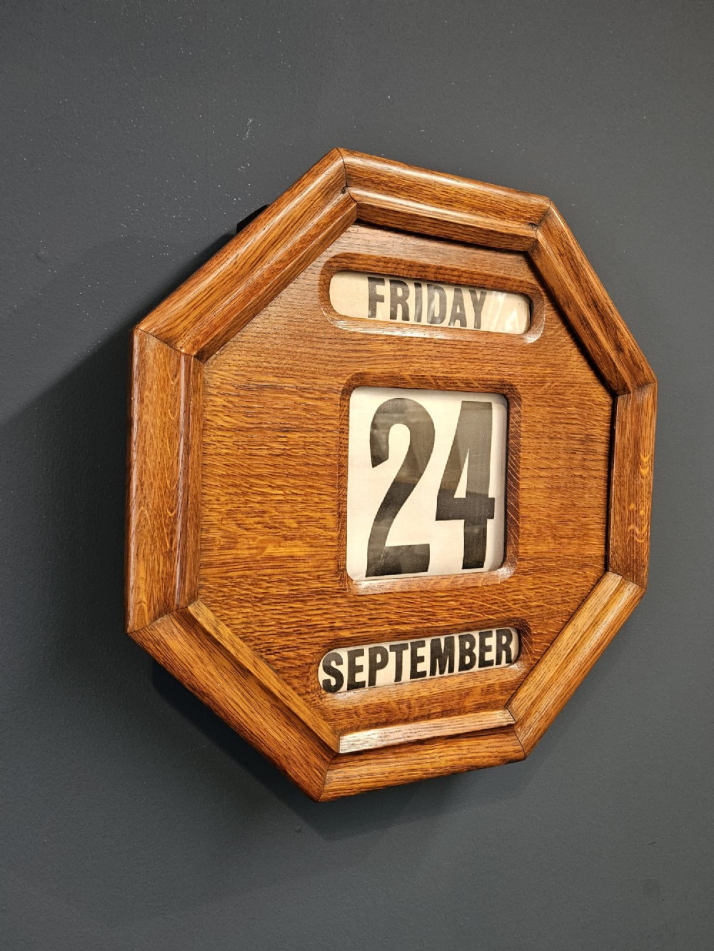 An octagonal Edwardian oak perpetual wall calendar with glazed apertures displaying the day, numerical date, and month on printed rollers. View III