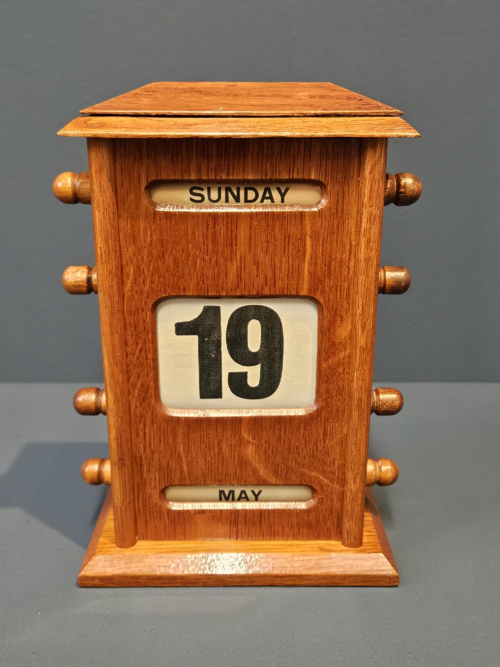 A golden oak perpetual desk calendar featuring side turning knobs and printed aperture windows displaying the day, date, and month.
