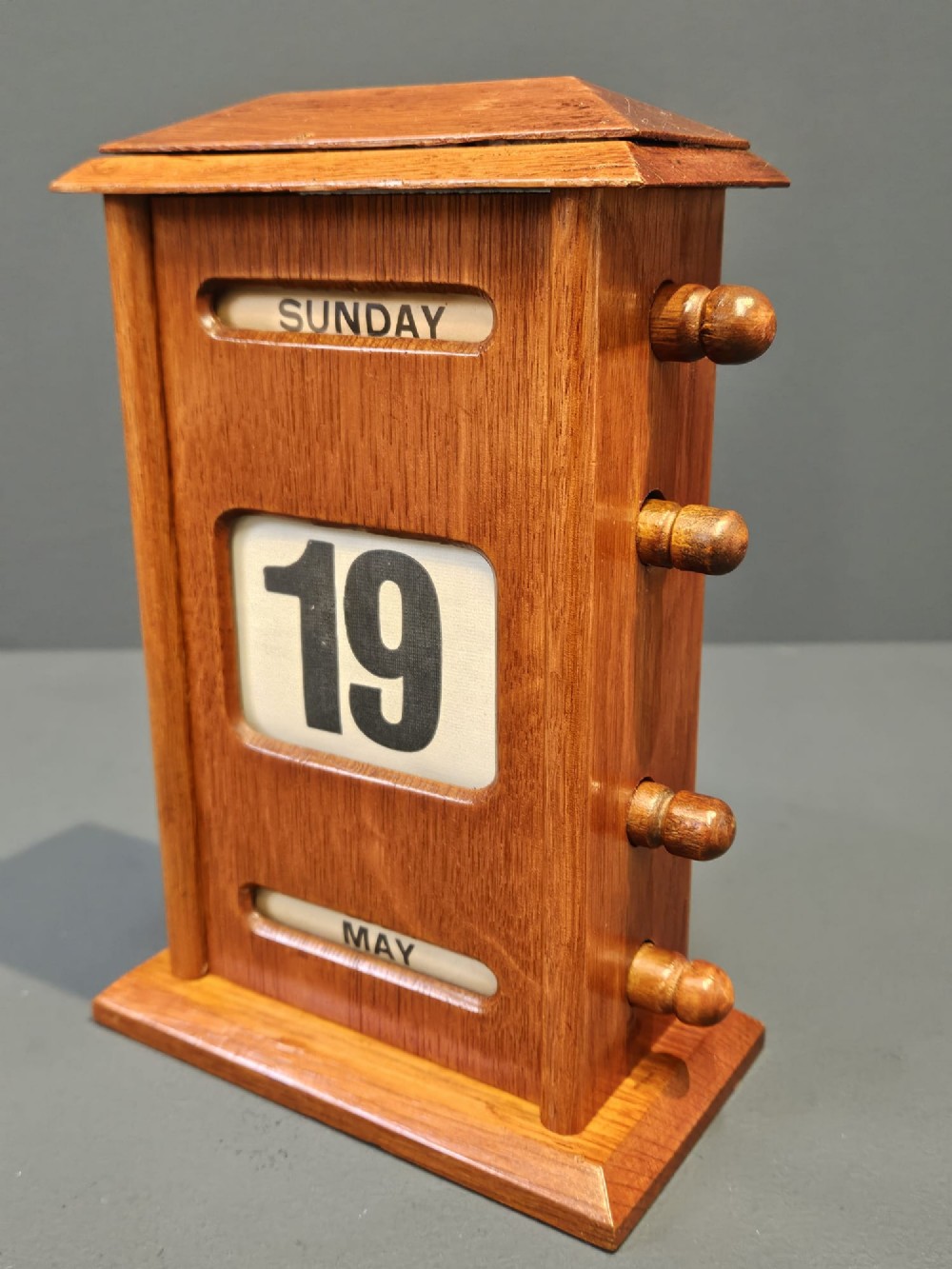 A golden oak perpetual desk calendar featuring side turning knobs and printed aperture windows displaying the day, date, and month. View II