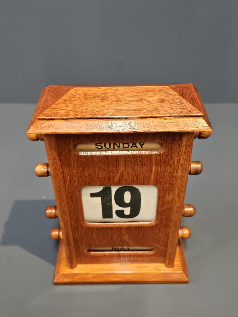 A golden oak perpetual desk calendar featuring side turning knobs and printed aperture windows displaying the day, date, and month. View IV