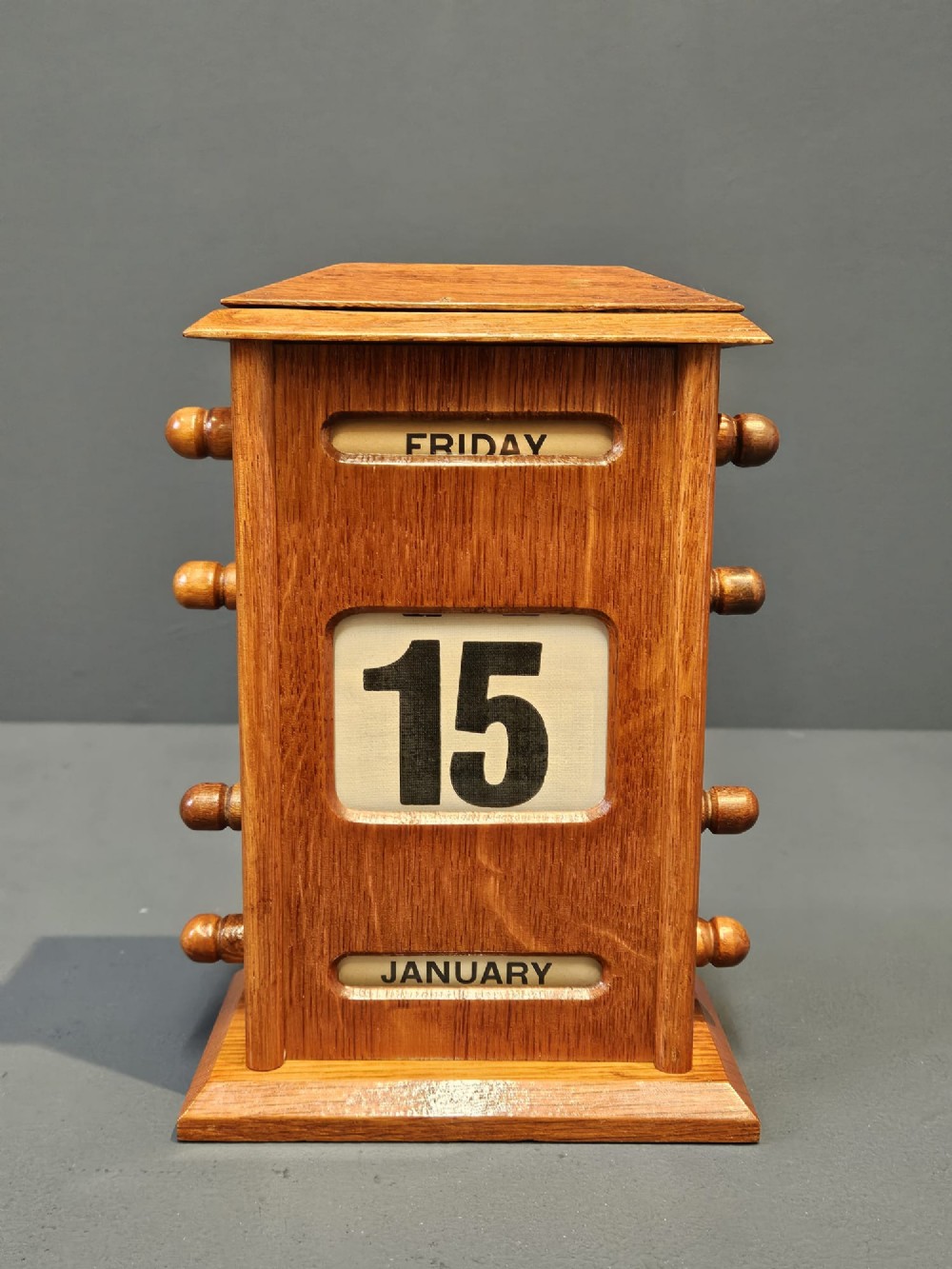 A golden oak perpetual desk calendar featuring side turning knobs and printed aperture windows displaying the day, date, and month. View VI