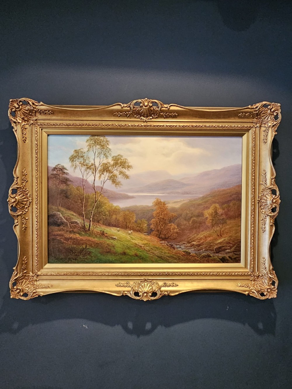 A Victorian landscape oil painting depicting a Lake District scene with hills and trees, enclosed in an ornate gold gilt frame. View VI