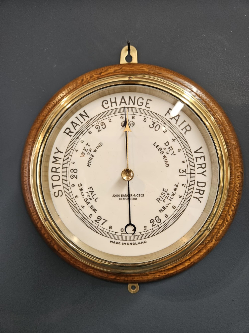 A circular Victorian brass bulkhead aneroid barometer with a cream dial mounted on a round wooden backplate. View II