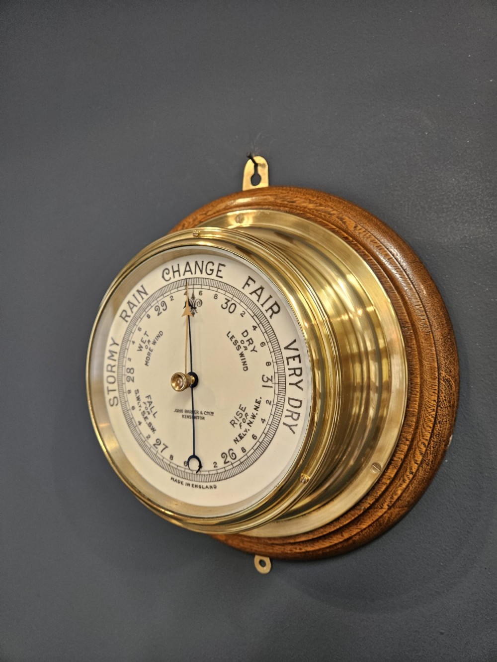 A circular Victorian brass bulkhead aneroid barometer with a cream dial mounted on a round wooden backplate. View III