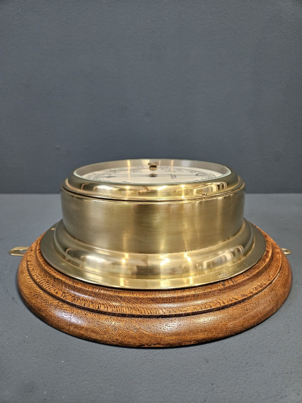 A circular Victorian brass bulkhead aneroid barometer with a cream dial mounted on a round wooden backplate. View V