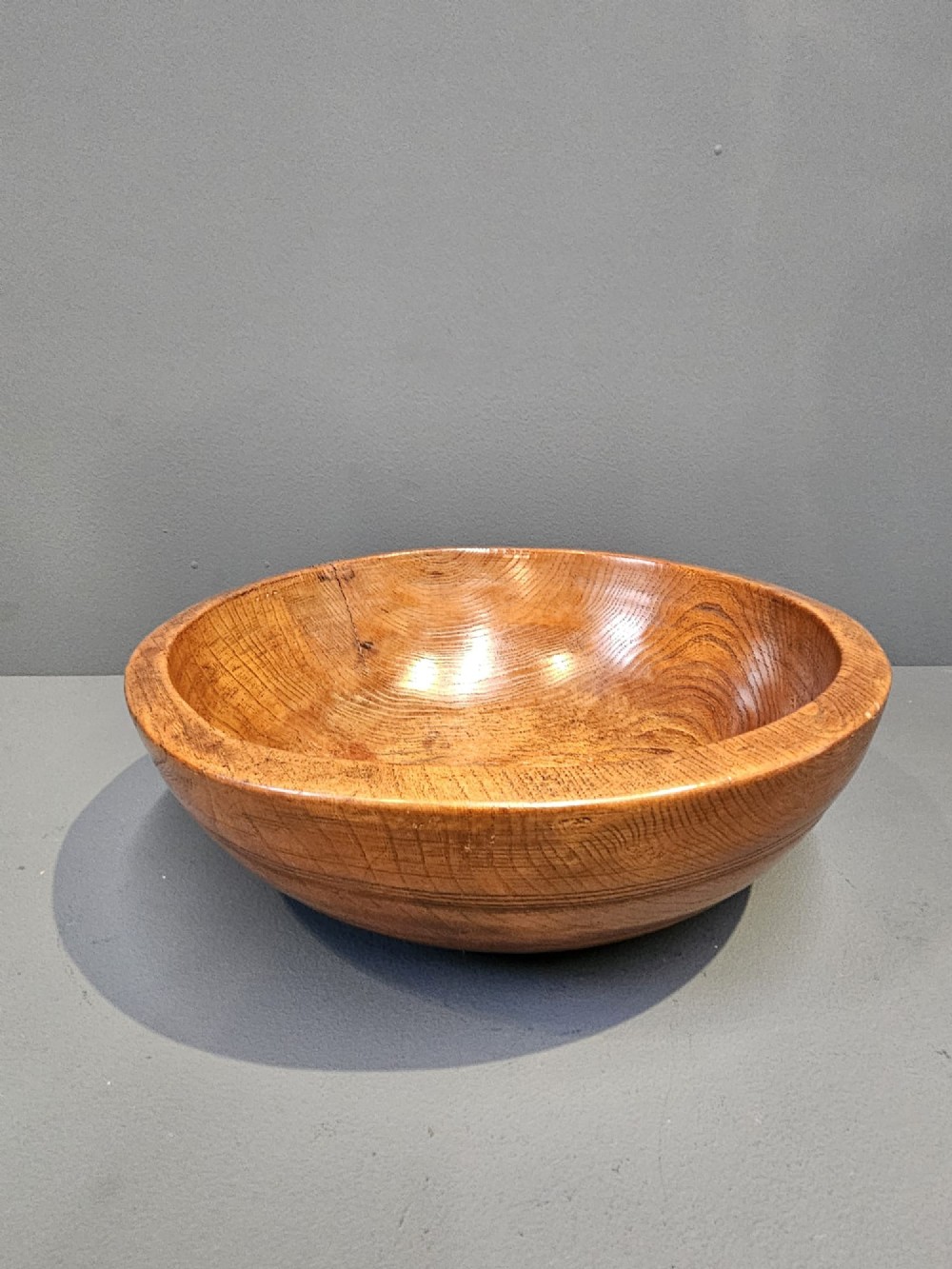 A turned early Victorian warm brown elm wood dairy bowl with a wide curved rim showing natural wood grain.