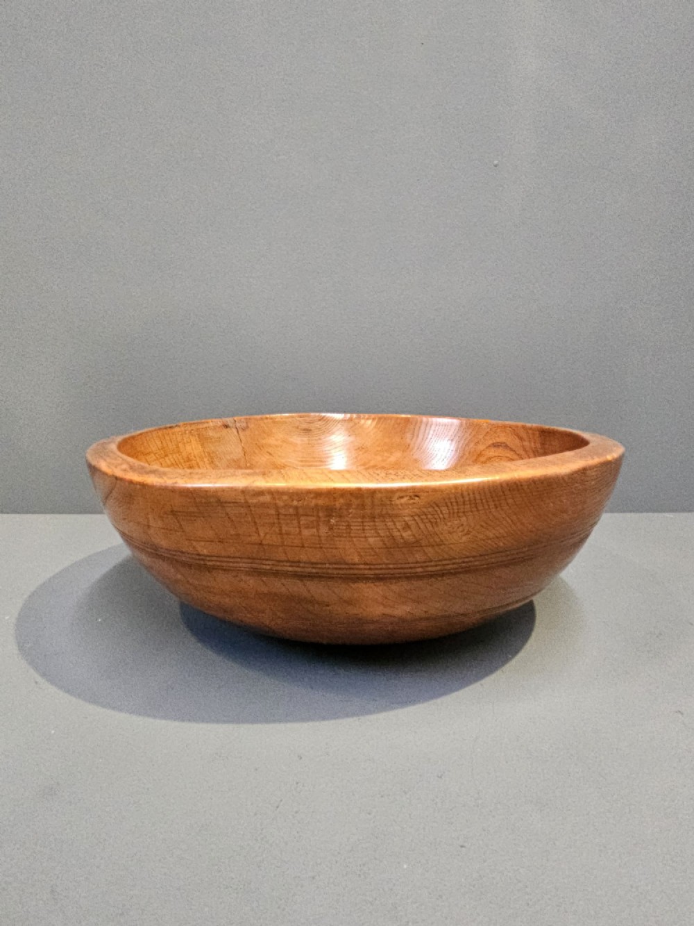A turned early Victorian warm brown elm wood dairy bowl with a wide curved rim showing natural wood grain. View II