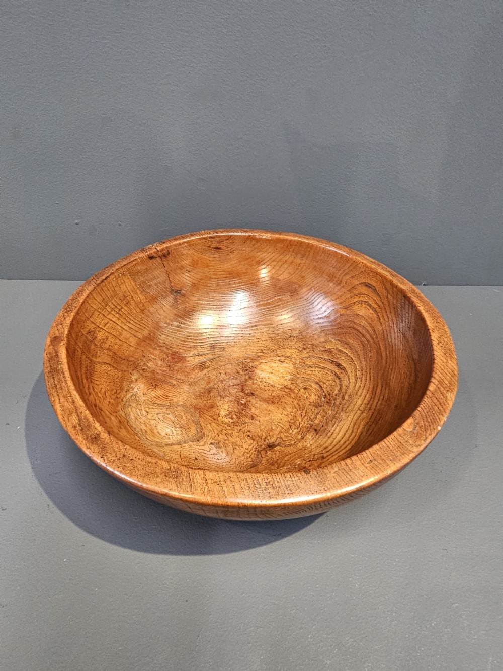 A turned early Victorian warm brown elm wood dairy bowl with a wide curved rim showing natural wood grain. View III