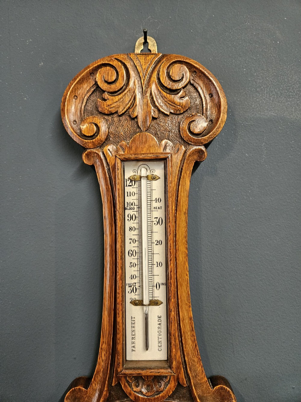 A carved oak banjo barometer featuring a upper spirit thermometer and a circular porcelain dial with an exposed skeletonised movement. View III