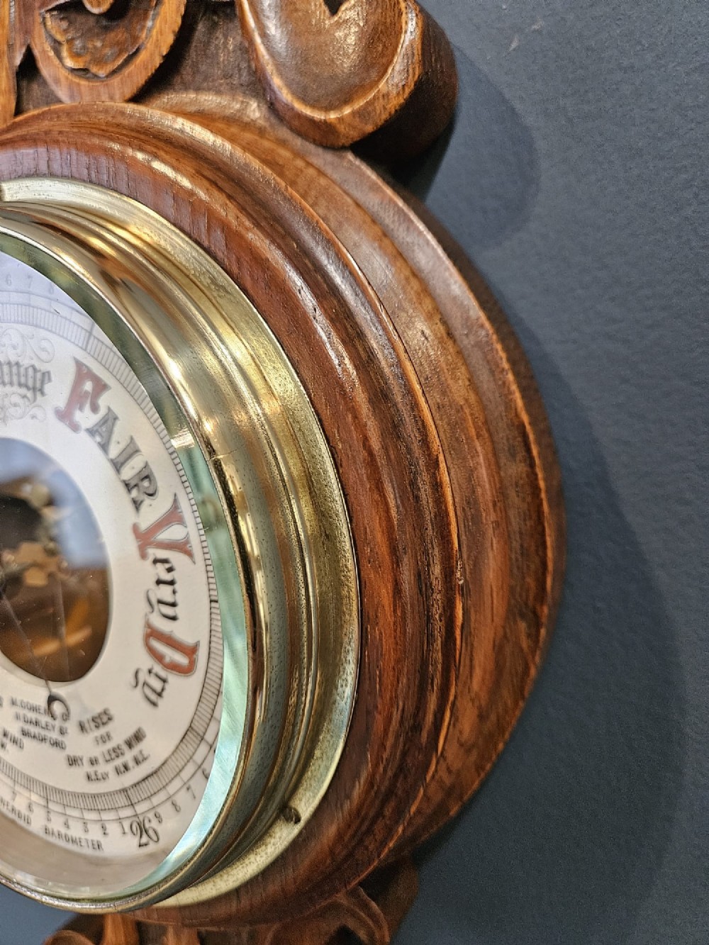 A carved oak banjo barometer featuring a upper spirit thermometer and a circular porcelain dial with an exposed skeletonised movement. View VII