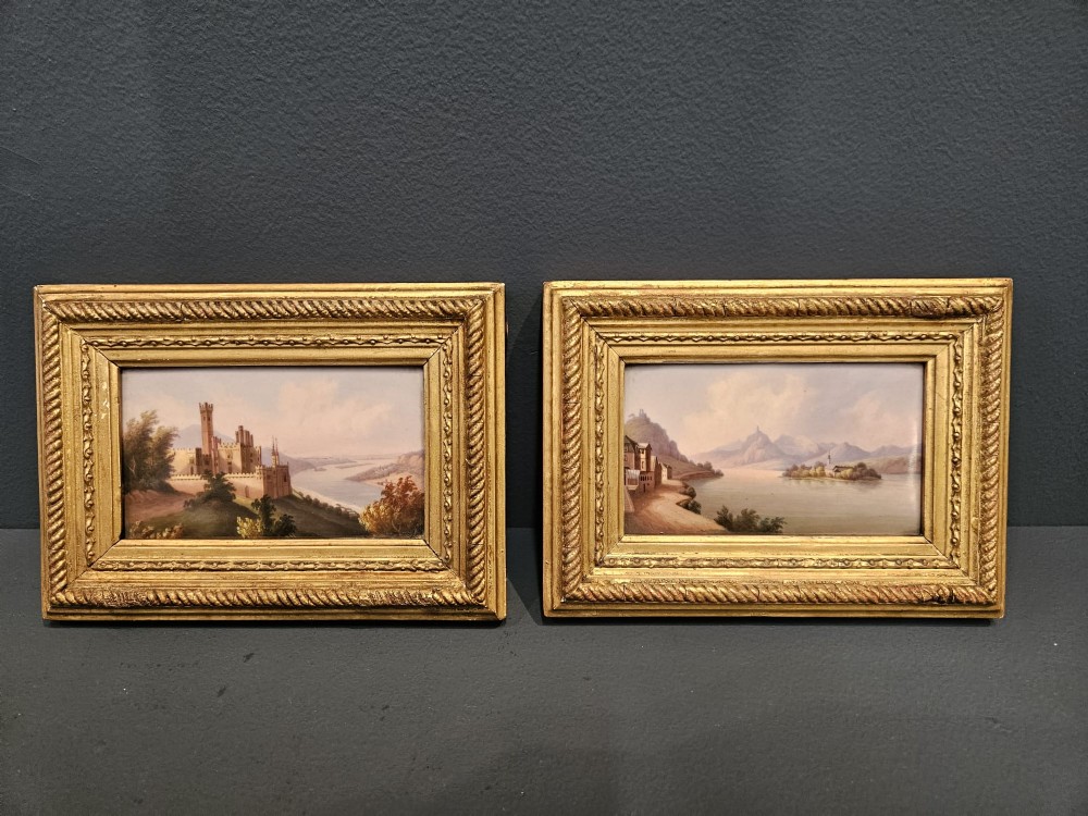 A pair of rectangular Victorian hand-painted porcelain plaques depicting European landscape scenes set within ornate giltwood rope-twist frames.