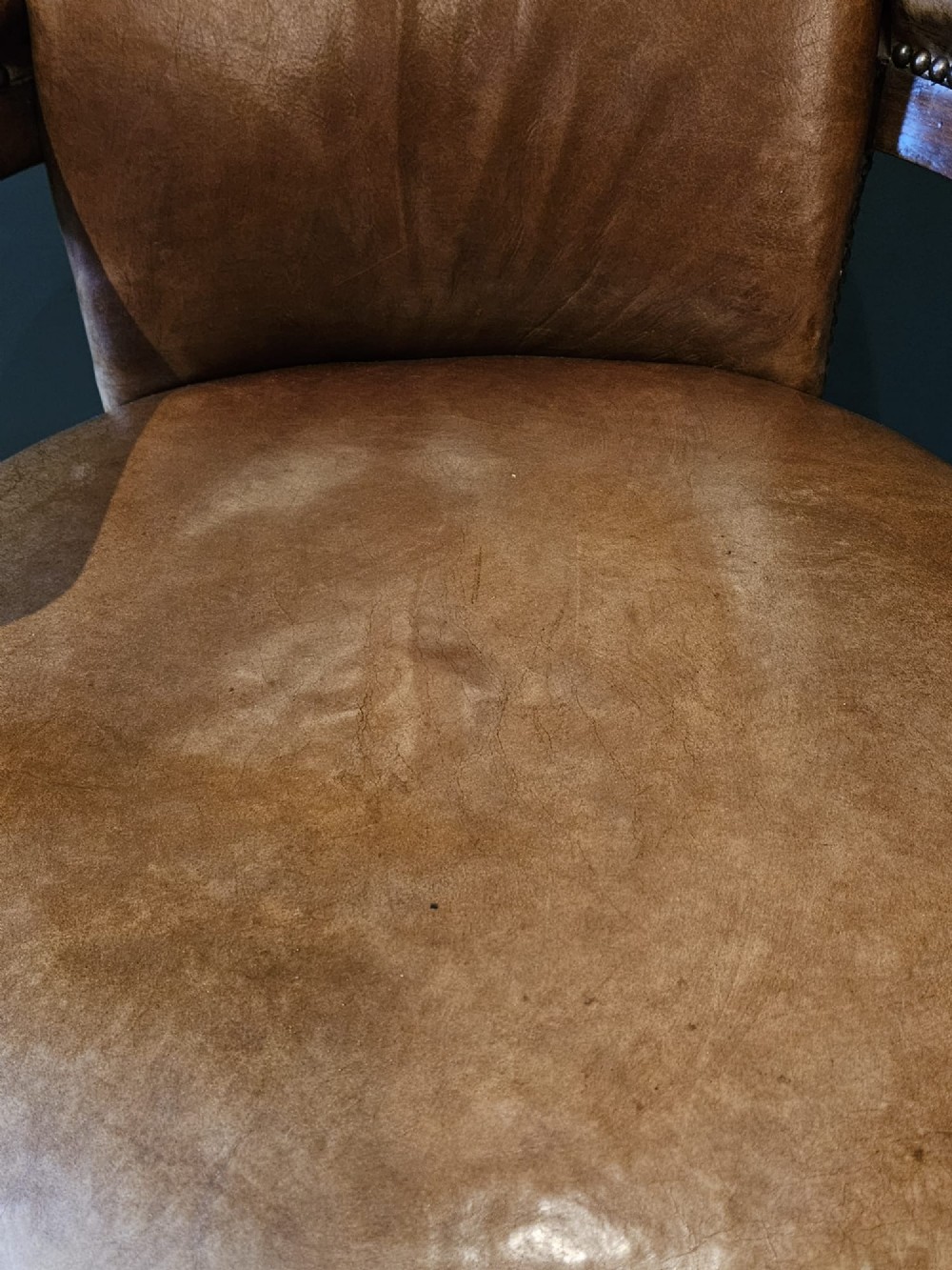 A Victorian revolving desk chair upholstered in tan hide leather with brass stud trim, curved armrests, and turned mahogany legs on brass castors. View VI