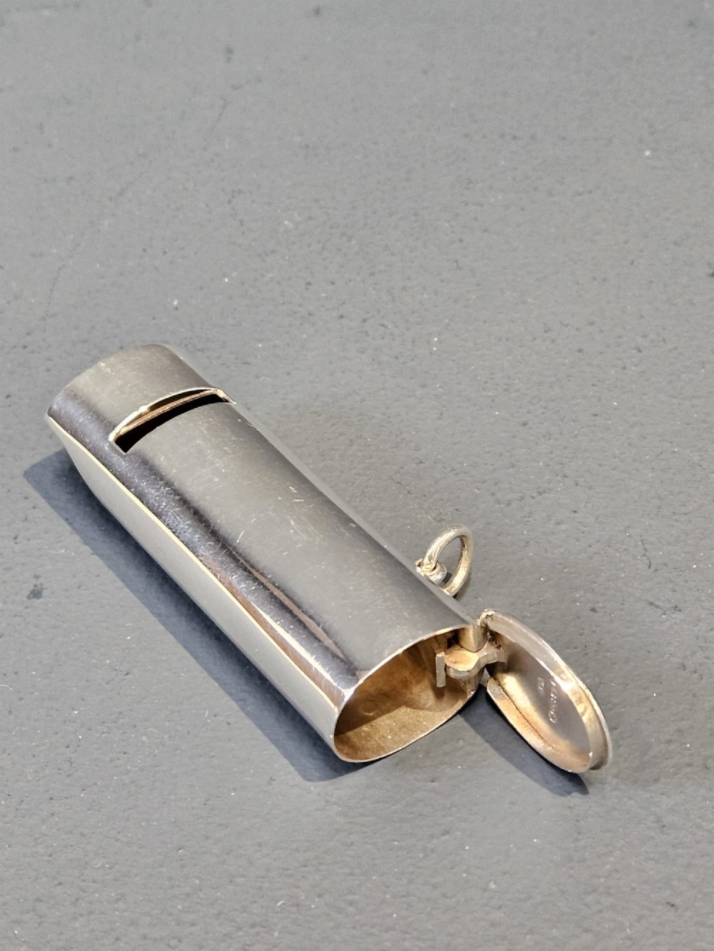 A polished Victorian sterling silver combined vesta case and whistle standing upright with a small suspension ring attached at the base. View V