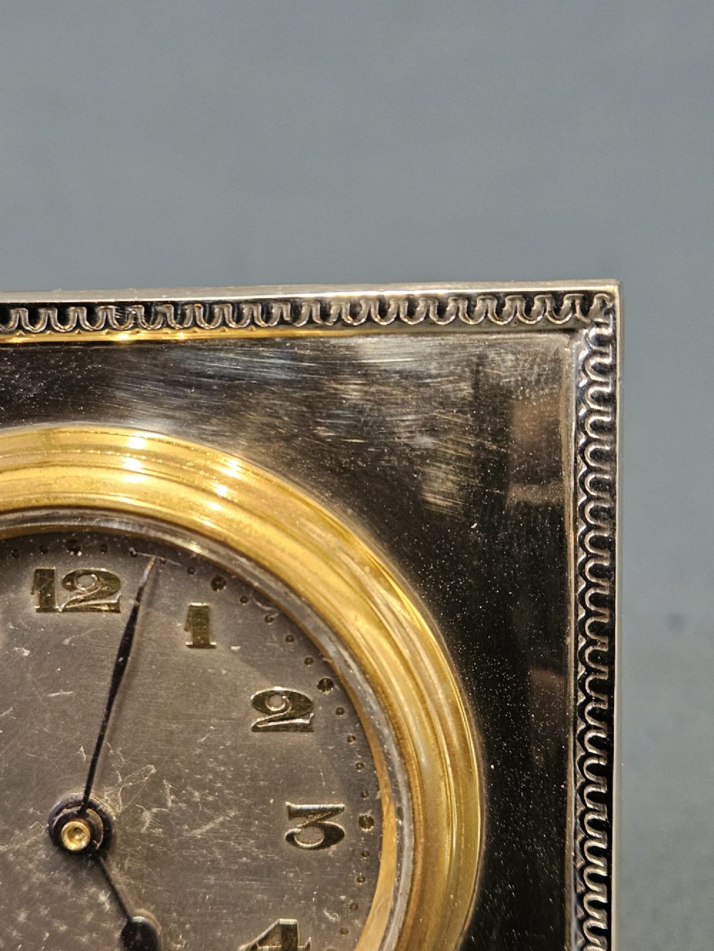 A square hallmarked sterling silver desk clock featuring a beaded outer frame, a brass inner bezel, and Arabic numerals on a metallic dial. View II