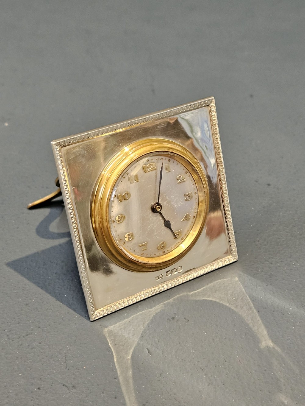 A square hallmarked sterling silver desk clock featuring a beaded outer frame, a brass inner bezel, and Arabic numerals on a metallic dial. View III