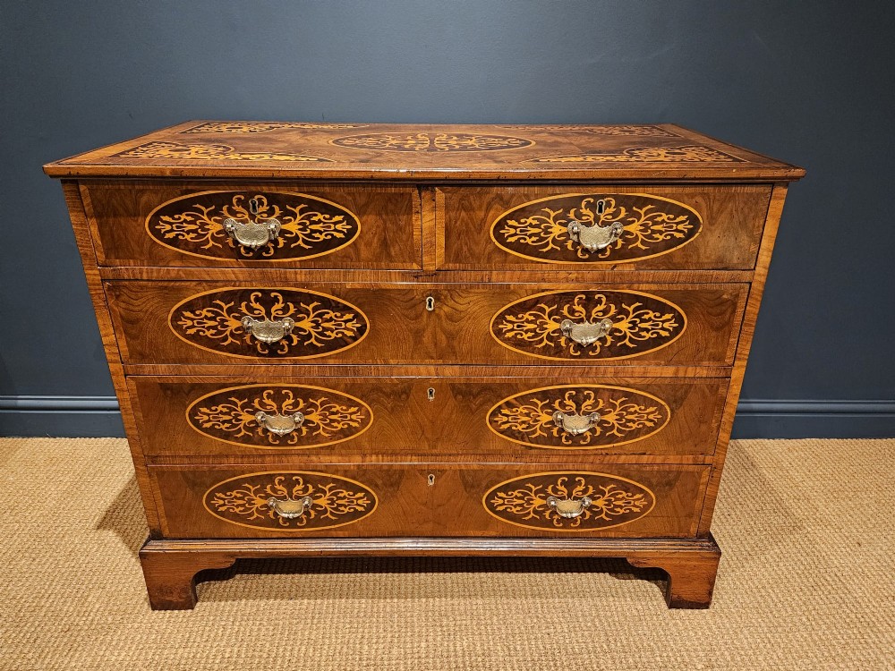 A George III period walnut chest of drawers featuring decorative oval marquetry inlays across four drawer fronts and brass handles, resting on bracket feet.